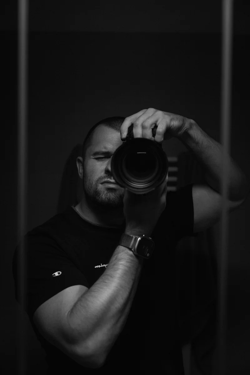 Lukáš Granatier with a camera to his eye, reflected in a mirror