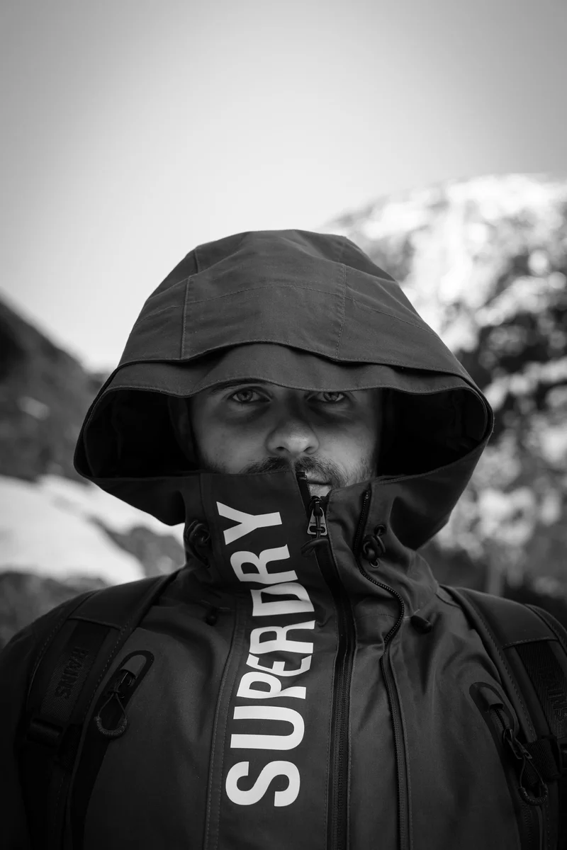 Lukáš Granatier in a hooded jacket, a snow-covered mountain slope behind him