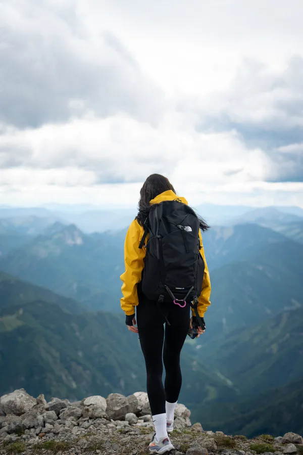 A person in a yellow jacket with a backpack on a rocky ridge above the mountains