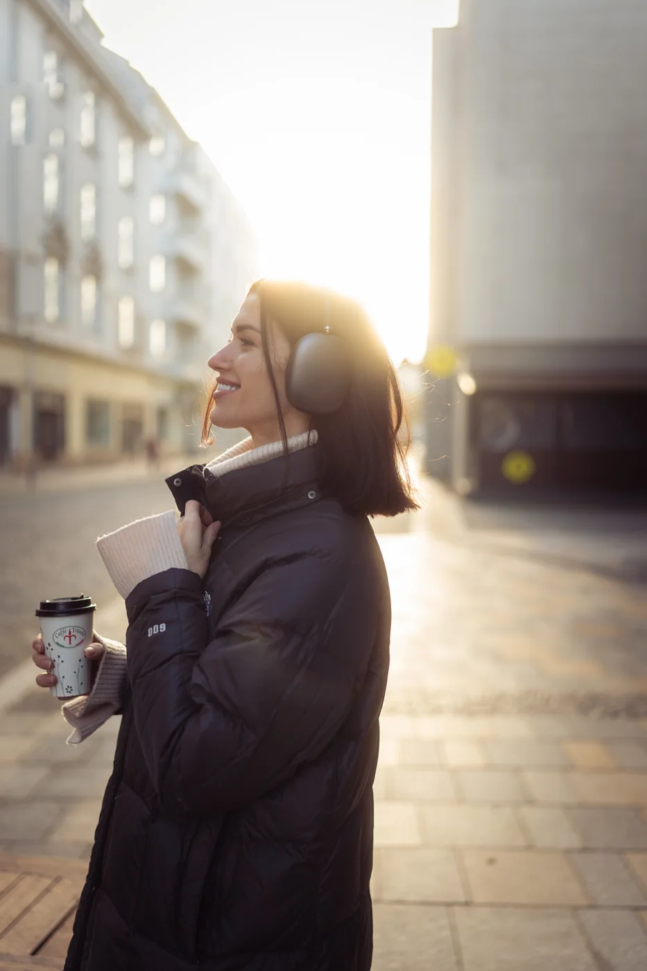 A woman holding a cup, backlit by sunlight on a city street