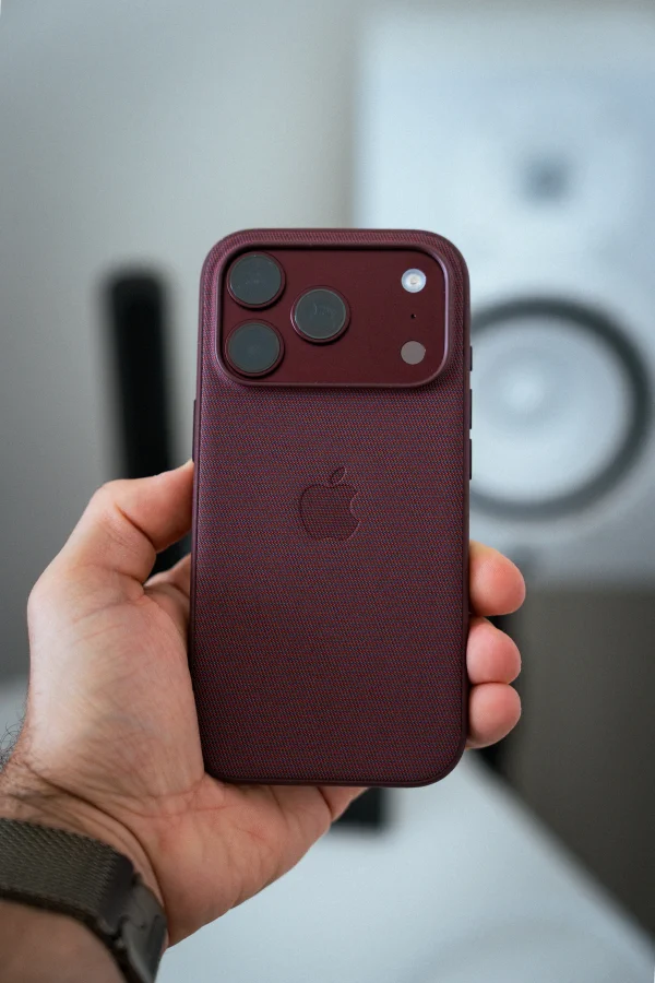 Telefon v tkaném vínovém pouzdře držený v dlani před rozostřeným studiovým reproduktorem