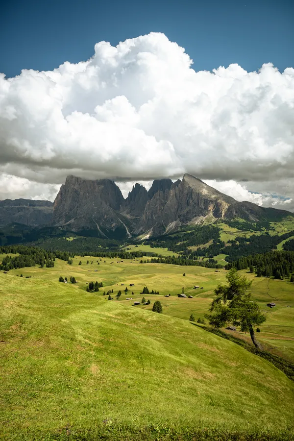 Green mountain meadows beneath a rocky massif and prominent white clouds