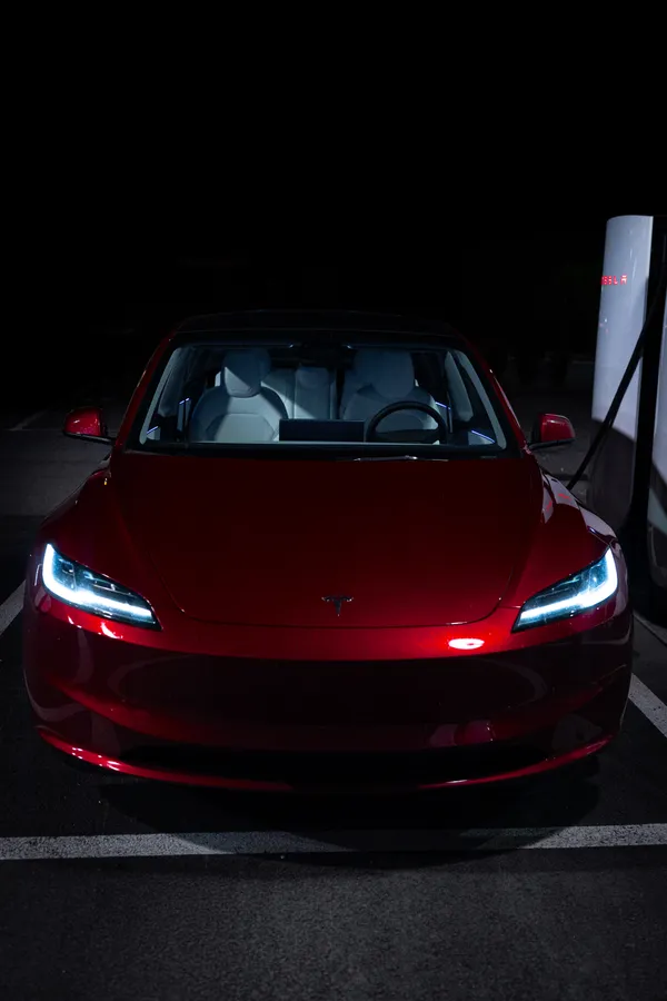 A red car with illuminated headlights at a charging point at night