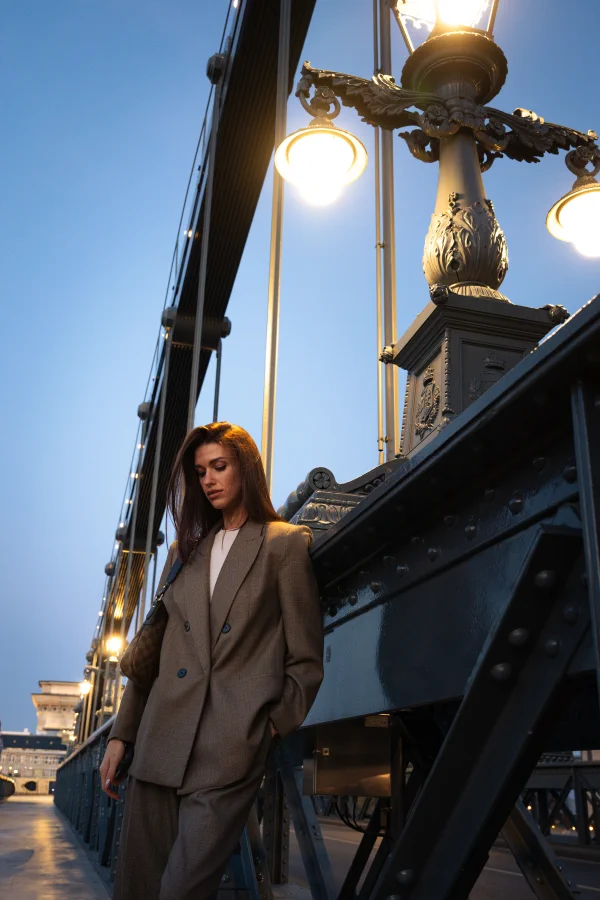 A portrait of a woman in a suit on a bridge with ornate lit lamps