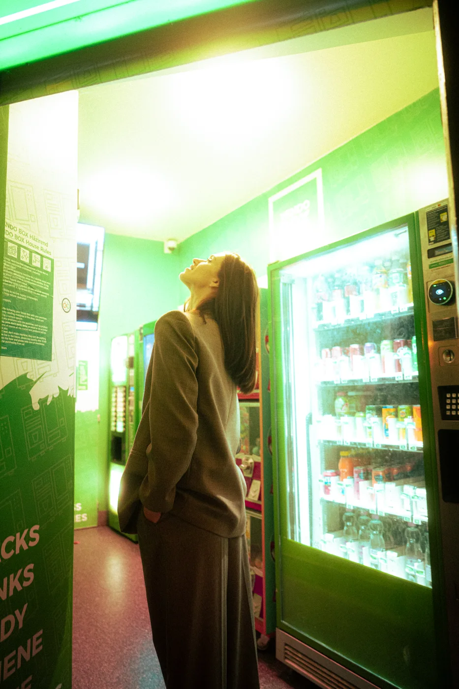 A person beside a green-lit vending machine at night