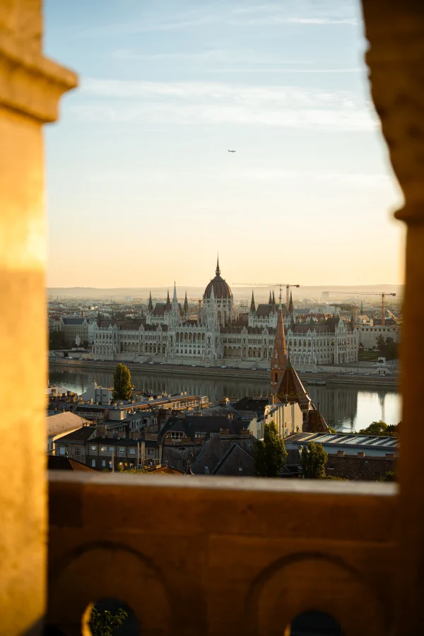 A historic parliament building above the river, framed by a stone arch in morning light
