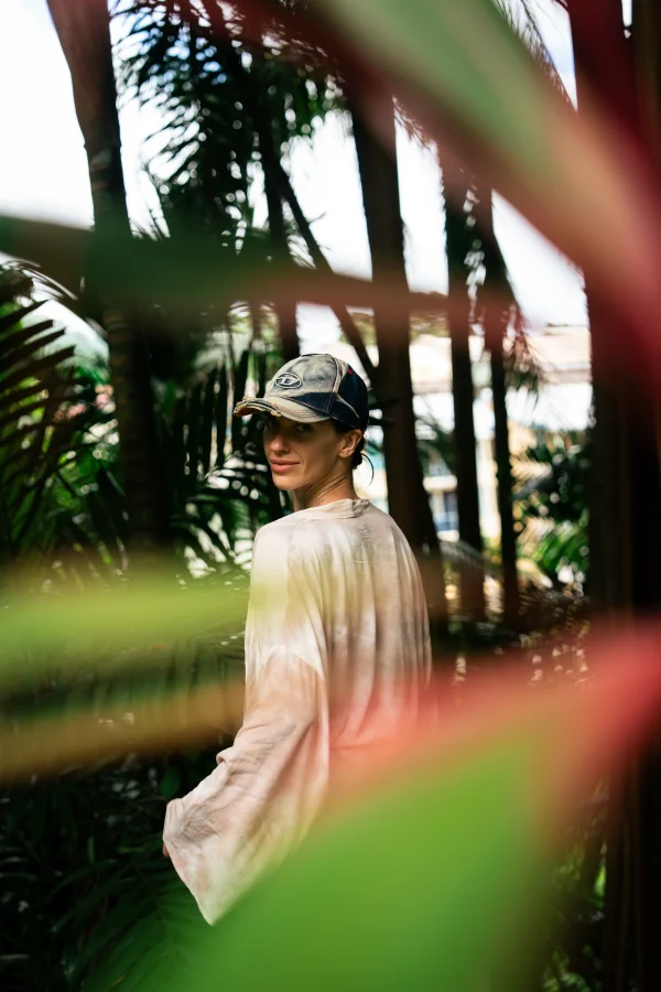 A portrait of a woman in a cap looking back over her shoulder, framed by palm fronds