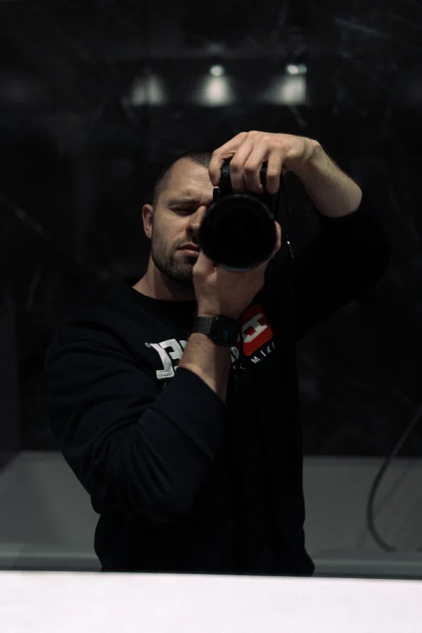 A reflection of the photographer with a camera to his eye in a dark glossy surface